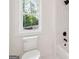 Bright bathroom with a white toilet, window, and marble-tiled shower with black fixtures at 3920 Clifton Hill Ct, Cumming, GA 30040