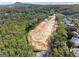Aerial view of construction in progress, showing a street and partially cleared land surrounded by lush trees at 3920 Clifton Hill Ct, Cumming, GA 30040