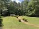 Large backyard with a brick pathway leading to a pergola and lush trees at 595 Huiet Dr, Mcdonough, GA 30252