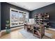 Home office with dark blue walls, wood floors, large window, built-in bookshelves, and desk at 13385 Bishops Ct, Roswell, GA 30075