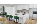 Modern white kitchen with an island, green bar stools, stainless steel appliances, and decorative backsplash at 1600 Cherry Hill Sw Ct, Conyers, GA 30094