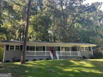 Ranch home with gray brick exterior, white trim, and a red front door, nestled amongst lush green trees at 3207 Cloverhurst Dr, East Point, GA 30344