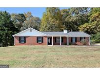 Brick ranch home with a covered porch, well-manicured lawn, and wooded backdrop at 138 Michelle Dr, Mcdonough, GA 30252