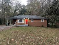 Brick ranch house with red door, landscaped yard, and driveway at 207 Howell Dr, Atlanta, GA 30331