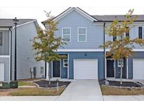 Two-story townhome with gray siding, a white garage door, and landscaping at 7121 Gladstone Cir, Lithonia, GA 30038