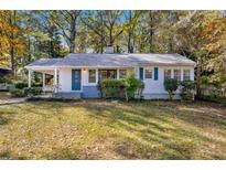 Charming white house with blue door, surrounded by lush green lawn and trees at 2627 Elsinore St, East Point, GA 30344