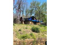 Stone and wood house needing repairs, covered with blue tarp, situated on a hill with trees at 1461 Hawthorne Way, Atlanta, GA 30344