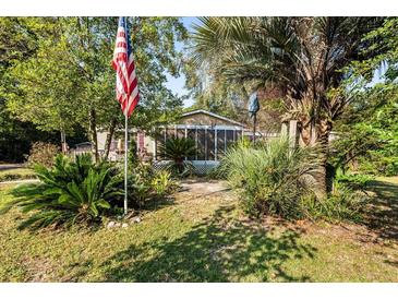 Single-story house with a screened porch, lush landscaping, and an American flag at 115 Galloway Ct, Moncks Corner, SC 29461