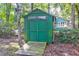 Green storage shed with double doors and wood ramp, nestled in a wooded backyard at 10 Trail Hollow Dr, Charleston, SC 29414