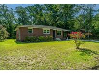 Brick ranch house with a spacious lawn, landscaped gardens and mature trees at 4418 Cindy Ln, North Charleston, SC 29418