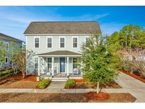 Two-story light green house with a front porch, rocking chairs, and manicured landscaping at 248 Great Lawn Dr, Summerville, SC 29486