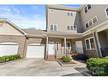 Tan three-story townhome with brick facade, attached garage, and front porch at 18819 Cloverstone Cir, Cornelius, NC 28031