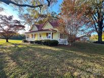Charming yellow farmhouse with red metal roof and rocking chairs on porch at 16409 Silver Rd, Oakboro, NC 28129