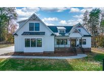 All-white charming farmhouse exterior with a brick base and a black metal roof at 3207 Frazier Dr, Claremont, NC 28610