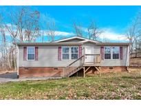 Gray mobile home with brick base, wooden deck and steps, set against a wooded backdrop at 633 Lhasa Apso Ln, Iron Station, NC 28080