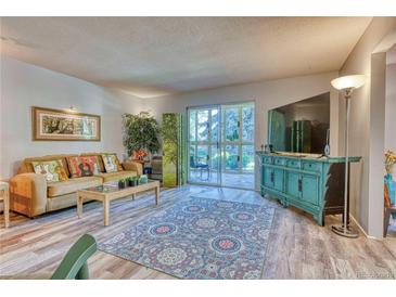 Living room with wood-look flooring, access to patio and large windows at 13609 E Cornell Ave # 107, Aurora, CO 80014