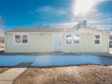 Ranch style home with light yellow exterior, partially snow-covered yard and a paved driveway at 775 Lashley St, Longmont, CO 80504