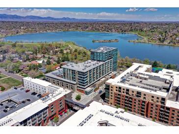 Aerial view of a modern condo building near a lake, with city skyline in the distance at 4200 W 17Th Ave # 235, Denver, CO 80204