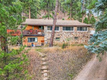 Rustic stone and wood home nestled in a wooded setting with multiple decks at 5200 Parmalee Gulch Rd, Indian Hills, CO 80454