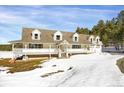 Charming two-story home with a wrap-around porch, nestled in a snowy landscape at 3619 Estates Cir, Larkspur, CO 80118