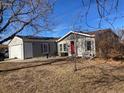 Gray house with red door, attached garage, and mature trees in front at 1103 Stage Dr, Fort Lupton, CO 80621