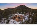 Exterior elevation of a home on a snowy, tree-covered hillside at sunset at 8838 Hillview Rd, Morrison, CO 80465