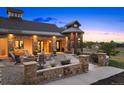 Elegant farmhouse exterior with stone patio and firepit at sunset at 5740 Flintwood Rd, Parker, CO 80134