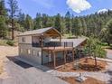 Exterior view showcasing a two-story home with balconies, front porch, and wooded surroundings at 2230 S Platte River Rd, Sedalia, CO 80135