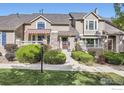 Tan two-story townhome with red door, landscaping, and striped awning at 6220 Salvia St, Arvada, CO 80403