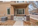 Front entrance of townhome with a covered porch, brick columns, and a white picket fence at 15536 W 64Th Loop # A, Arvada, CO 80007