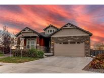 Two-story house with stone and beige siding, two-car garage, and landscaped yard at 10303 Pitkin Ct, Commerce City, CO 80022