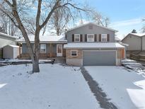 Two-story house with gray siding, attached garage, and snowy front yard at 13722 W 67Th Pl, Arvada, CO 80004