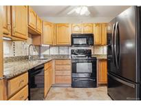 Updated kitchen with black appliances, granite countertops, and oak cabinetry at 585 S Alton Way # 4D, Denver, CO 80247