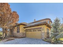 Exterior of house with stone accents and a paved driveway.Landscaped with trees at 7818 Vallagio Ln, Englewood, CO 80112