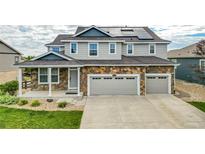 Two-story house with stone and gray siding, solar panels, and a two-car garage at 8686 S Buchanan Way, Aurora, CO 80016