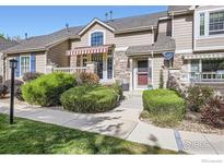 Tan two-story townhome with red door, landscaping, and striped awning at 6220 Salvia St, Arvada, CO 80403