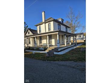 Two-story white brick home with a wraparound porch and landscaped yard at 201 W Walnut St, Waldron, IN 46182