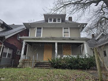 Two-story house needing renovation, featuring a front porch and boarded windows at 3609 E Washington St, Indianapolis, IN 46201