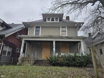 Two-story house needing renovation, featuring a front porch and boarded windows at 3609 E Washington St, Indianapolis, IN 46201