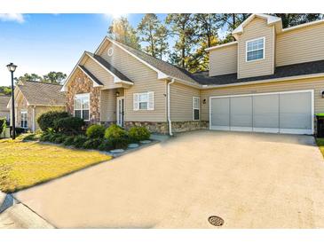 Tan house with stone accents and a two-car garage, featuring a well-maintained lawn at 4268 River Gate Ln., Little River, SC 29566