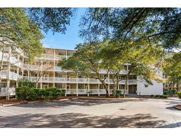 Exterior view of a multi-story condo building with balconies, lush trees, and parking at 415 Ocean Creek Dr. # 2236, Myrtle Beach, SC 29572