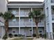 Two-story condo building with light gray siding, white trim, and palm trees at 4717 Wild Iris Dr. # 29-303, Myrtle Beach, SC 29577