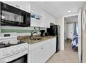 White kitchen with granite countertops, black appliances, and open shelving at 2001 S Ocean Blvd. # 1506, Myrtle Beach, SC 29577