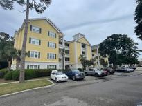 Three-story building with yellow exterior, ample parking, and landscaping at 601 N Hillside Dr. # 2123, North Myrtle Beach, SC 29582