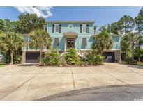 Attractive two-story home with a light teal exterior, lush landscaping, and a circular driveway at 119 Cockle Shell Ct., Pawleys Island, SC 29585