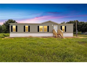 Single-wide manufactured home with gray siding, wooden steps, and a grassy yard at 10109 Old Spanish Trl, Polk City, FL 33868