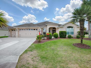 One-story house with beige exterior, two-car garage, and lush landscaping at 1751 Ashwood Run, The Villages, FL 32162