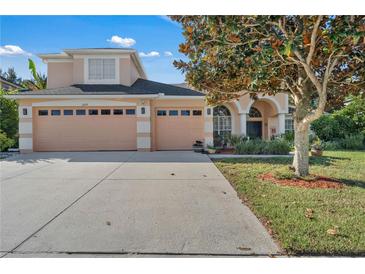 Two-story house with peach walls, three-car garage, and manicured lawn at 13129 Coldwater Loop, Clermont, FL 34711