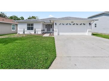 White house with gray roof, two-car garage, and well-manicured lawn at 32857 Timberwood Dr, Leesburg, FL 34748