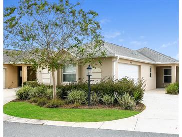Tan two-car garage villa with a landscaped yard and walkway at 928 Nuthatch Ave, The Villages, FL 32163